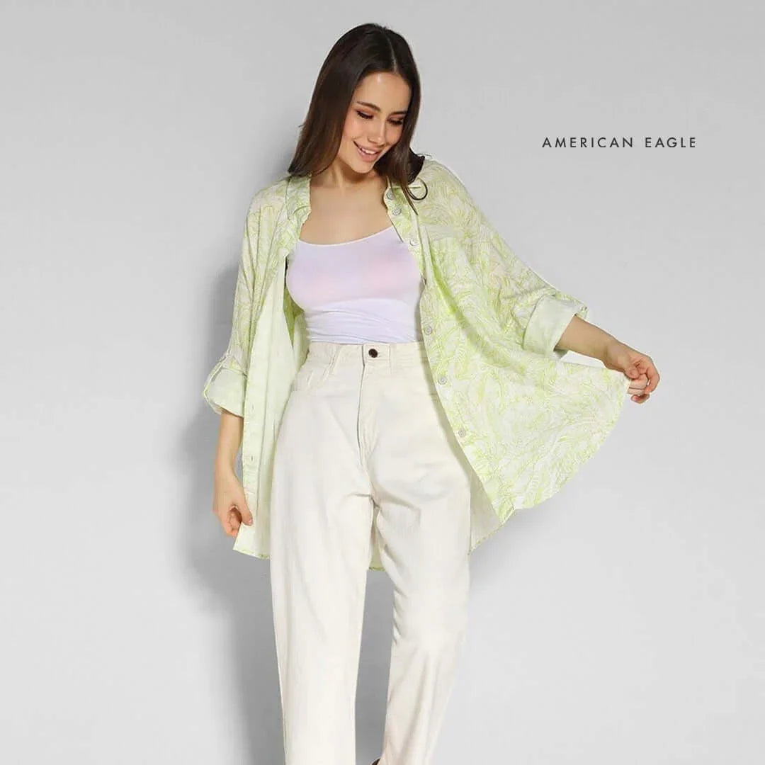 Woman wearing AMERICAN EAGLE printed oversized shirt with cream-colored pants, showcasing a casual stylish look.