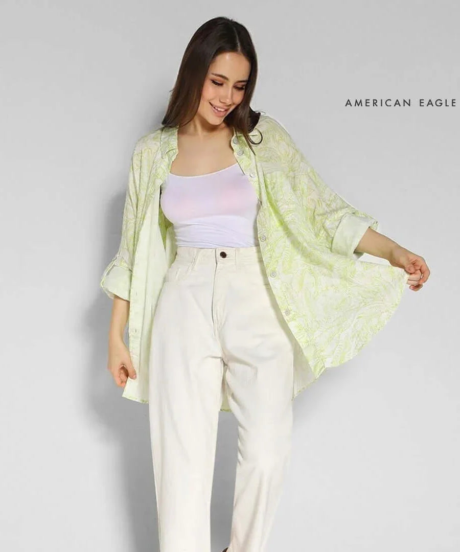 Woman wearing AMERICAN EAGLE printed oversized shirt with cream-colored pants, showcasing a casual stylish look.